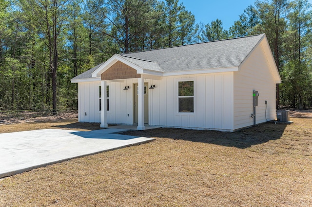 modern farmhouse with central air condition unit, roof with shingles, a front lawn, board and batten siding, and a patio area