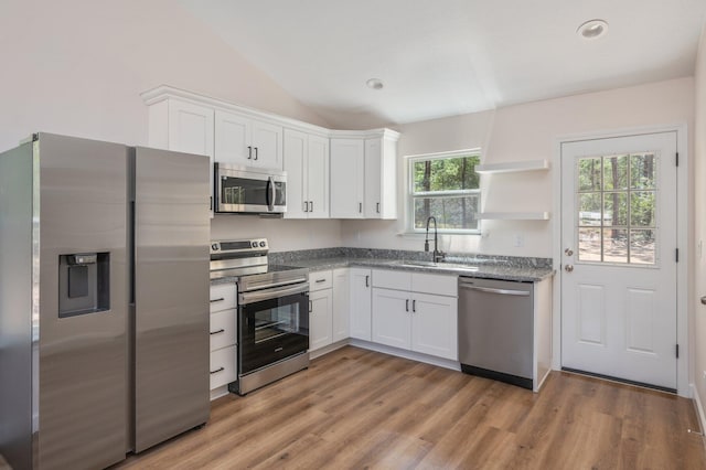 kitchen featuring stainless steel appliances, lofted ceiling, light wood-style floors, white cabinets, and a sink