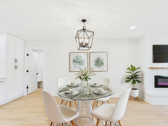 dining space featuring light wood finished floors, a glass covered fireplace, recessed lighting, and an inviting chandelier