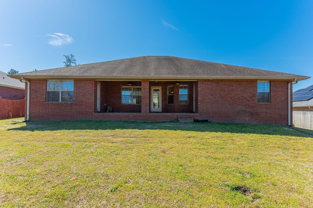 back of property featuring ceiling fan, brick siding, a lawn, and fence