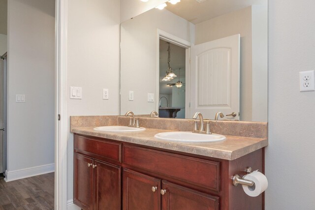 bathroom with double vanity, wood finished floors, a sink, and baseboards