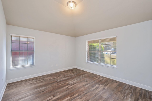 spare room with dark wood-style flooring, vaulted ceiling, and baseboards