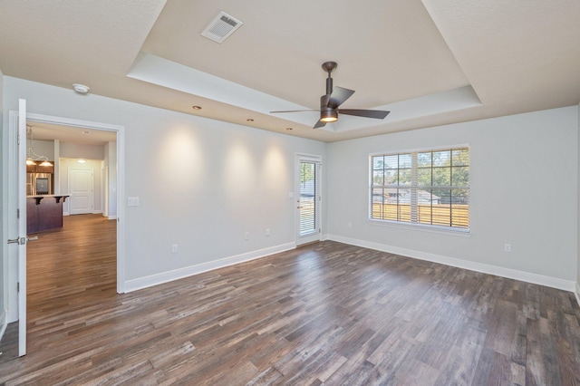 empty room with a tray ceiling, dark wood-style flooring, visible vents, and baseboards