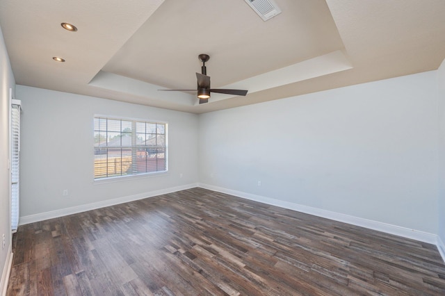 unfurnished room featuring visible vents, baseboards, a ceiling fan, dark wood-type flooring, and a tray ceiling