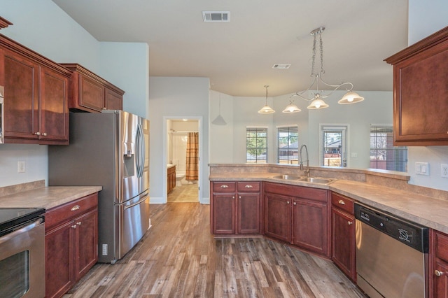 kitchen with stainless steel appliances, visible vents, hanging light fixtures, a sink, and wood finished floors