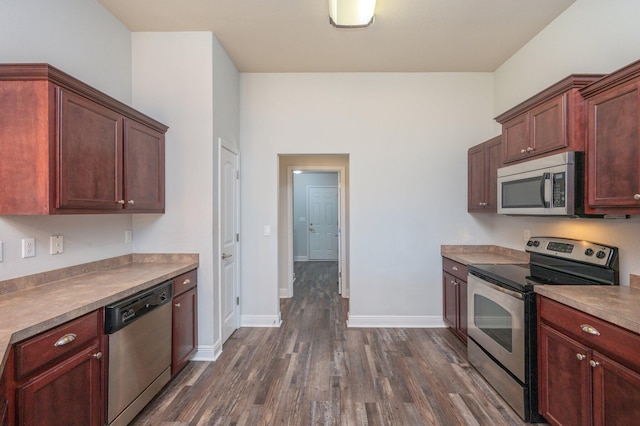 kitchen with appliances with stainless steel finishes, dark wood-style flooring, and baseboards