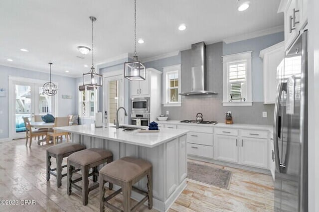 kitchen with a kitchen island with sink, a sink, light countertops, appliances with stainless steel finishes, and wall chimney exhaust hood