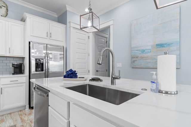 kitchen with a sink, stainless steel appliances, ornamental molding, and white cabinetry