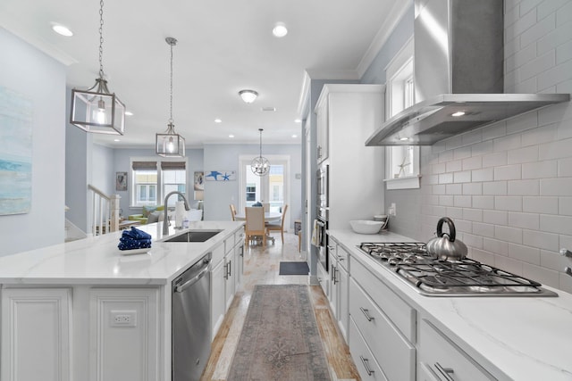 kitchen with crown molding, wall chimney range hood, light wood-style flooring, appliances with stainless steel finishes, and a sink