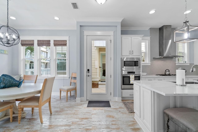 kitchen featuring visible vents, stainless steel appliances, crown molding, wall chimney range hood, and backsplash