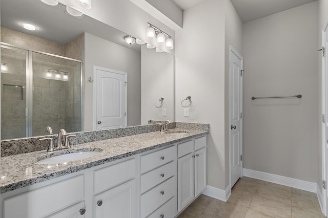 bathroom featuring double vanity, a shower stall, baseboards, and a sink