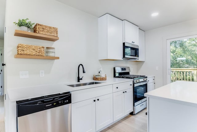 kitchen featuring appliances with stainless steel finishes, open shelves, a sink, and light countertops