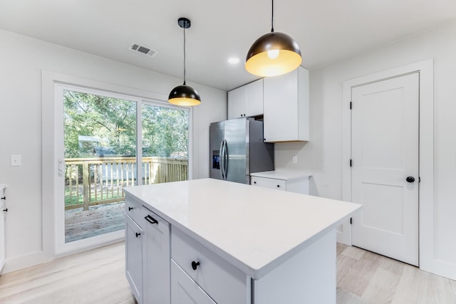 kitchen featuring light wood finished floors, stainless steel fridge with ice dispenser, a center island, light countertops, and white cabinetry