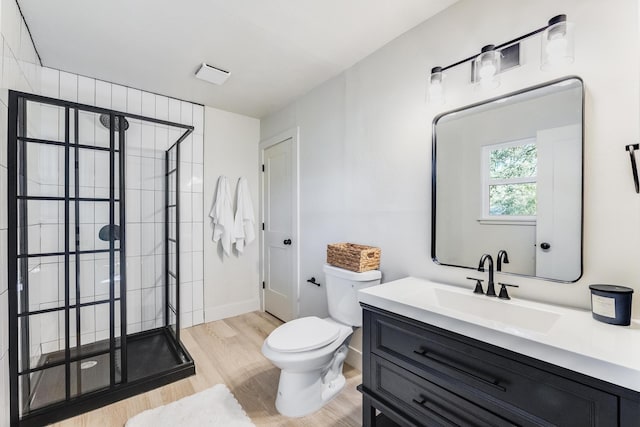 bathroom featuring toilet, wood finished floors, vanity, baseboards, and a tile shower