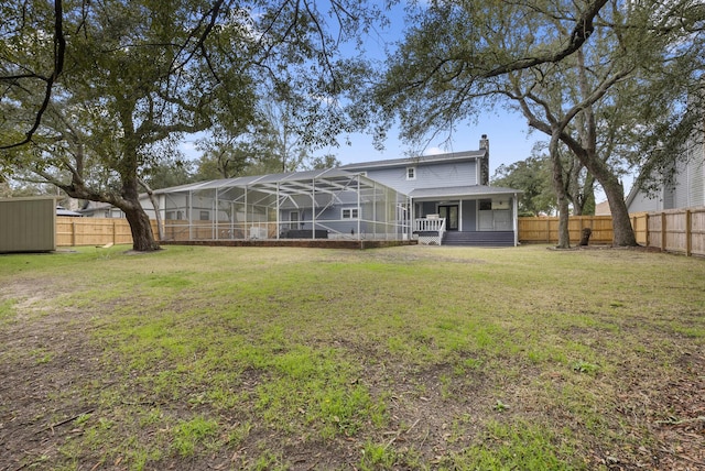 back of house with glass enclosure, a chimney, a lawn, and a fenced backyard