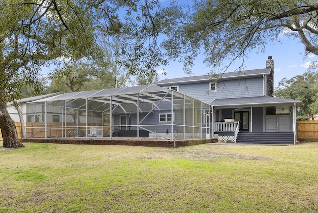 rear view of house with a lawn, a chimney, glass enclosure, and fence