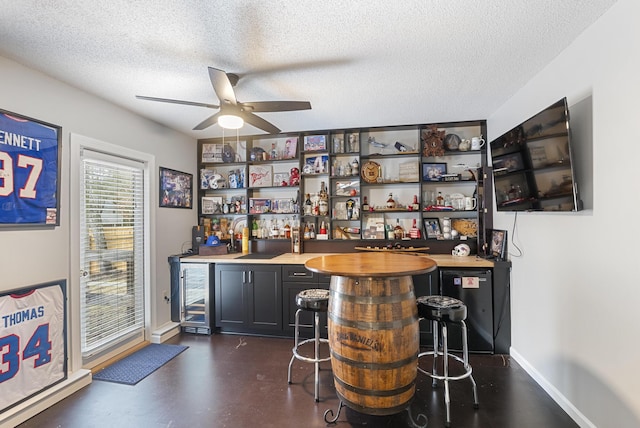 bar with baseboards, beverage cooler, wet bar, a textured ceiling, and a ceiling fan