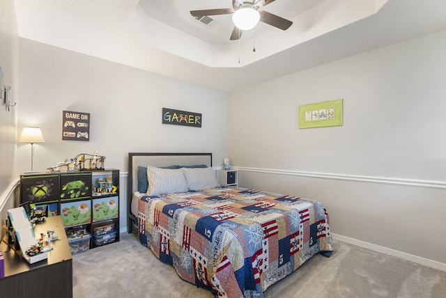 carpeted bedroom featuring visible vents, baseboards, a tray ceiling, and a ceiling fan