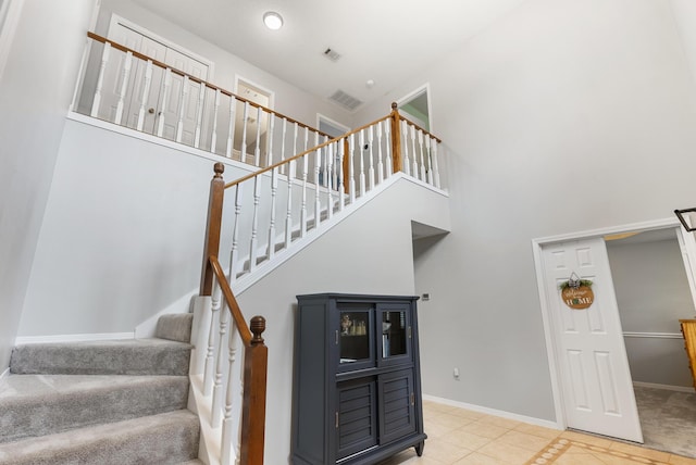 staircase with tile patterned flooring, visible vents, baseboards, and a towering ceiling