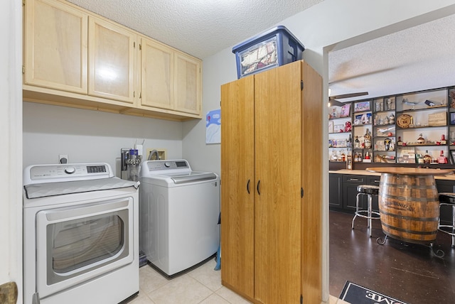 clothes washing area with washer and dryer, cabinet space, a textured ceiling, and indoor bar