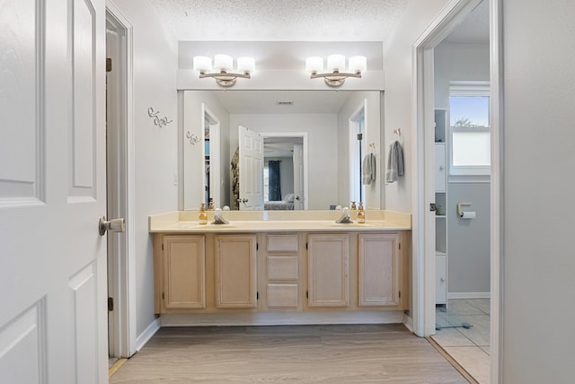 bathroom featuring wood finished floors, a sink, a textured ceiling, and double vanity