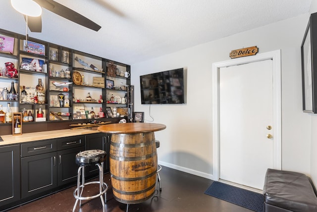 bar featuring finished concrete flooring, bar area, baseboards, a textured ceiling, and a ceiling fan