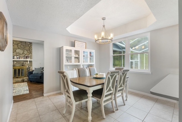 dining space with baseboards, light tile patterned floors, a notable chandelier, a textured ceiling, and a raised ceiling