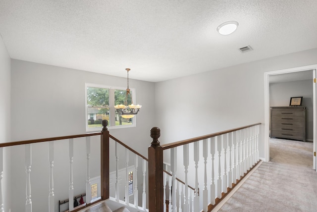 corridor with visible vents, a chandelier, carpet floors, an upstairs landing, and a textured ceiling