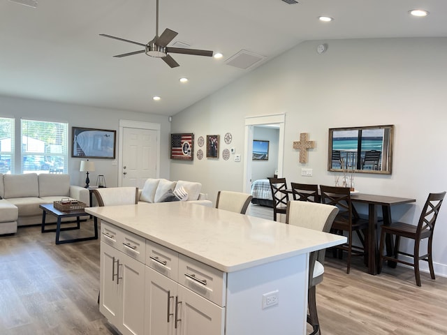 kitchen with a breakfast bar, a kitchen island, light wood-style floors, open floor plan, and white cabinets