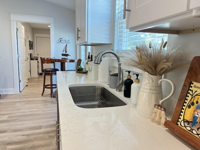 details with light wood-style floors, white cabinets, a sink, and light stone counters