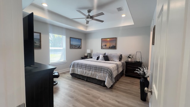 bedroom featuring visible vents, baseboards, light wood-style flooring, a tray ceiling, and recessed lighting