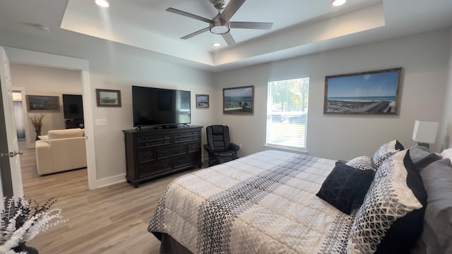 bedroom featuring light wood finished floors, baseboards, ceiling fan, a tray ceiling, and recessed lighting