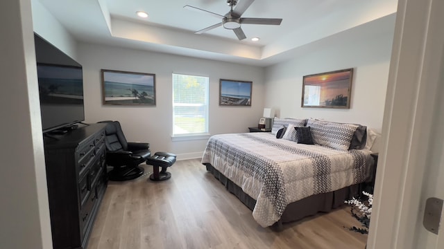 bedroom with light wood-style floors, recessed lighting, a raised ceiling, and baseboards