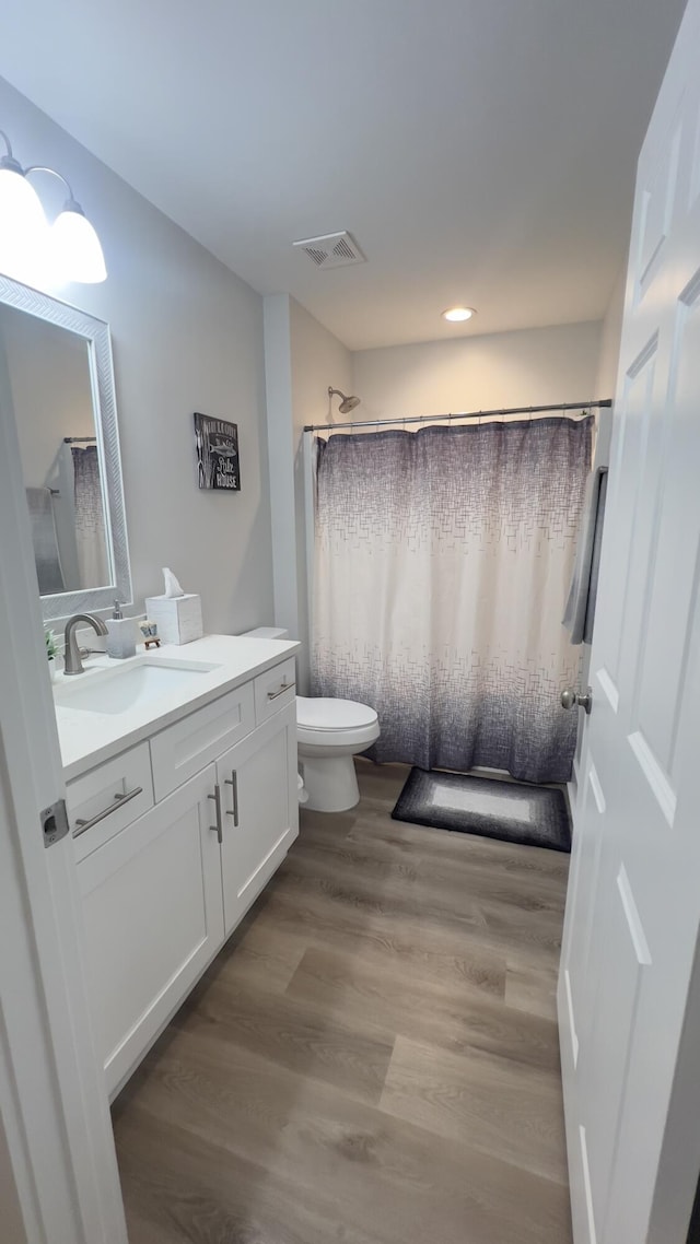 bathroom with visible vents, a shower with shower curtain, toilet, wood finished floors, and vanity