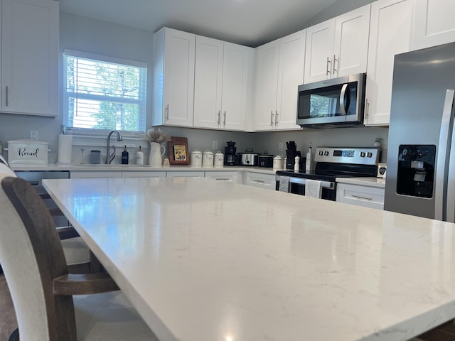 kitchen with light stone counters, a kitchen breakfast bar, a center island, stainless steel appliances, and a sink