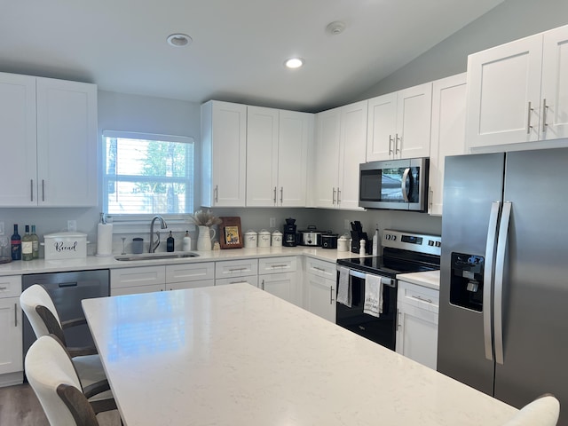 kitchen featuring appliances with stainless steel finishes, a sink, a breakfast bar, and white cabinetry