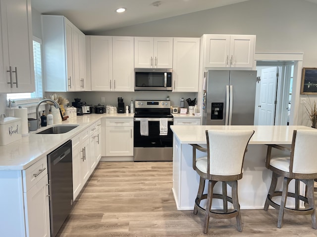 kitchen featuring lofted ceiling, stainless steel appliances, a sink, white cabinetry, and a kitchen breakfast bar