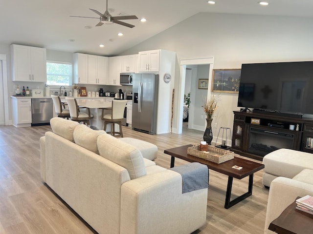 living area featuring high vaulted ceiling, recessed lighting, a ceiling fan, light wood finished floors, and a glass covered fireplace