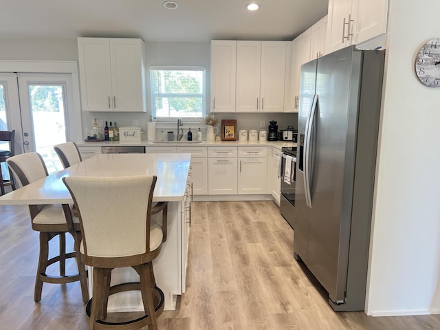 kitchen featuring light countertops, appliances with stainless steel finishes, white cabinets, a sink, and a kitchen breakfast bar