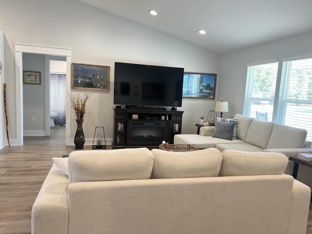 living room with lofted ceiling, recessed lighting, baseboards, light wood-style floors, and a glass covered fireplace