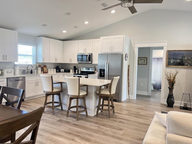 kitchen with light wood finished floors, a breakfast bar area, light countertops, appliances with stainless steel finishes, and white cabinets