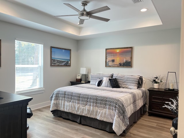 bedroom with light wood finished floors, baseboards, a raised ceiling, a ceiling fan, and recessed lighting