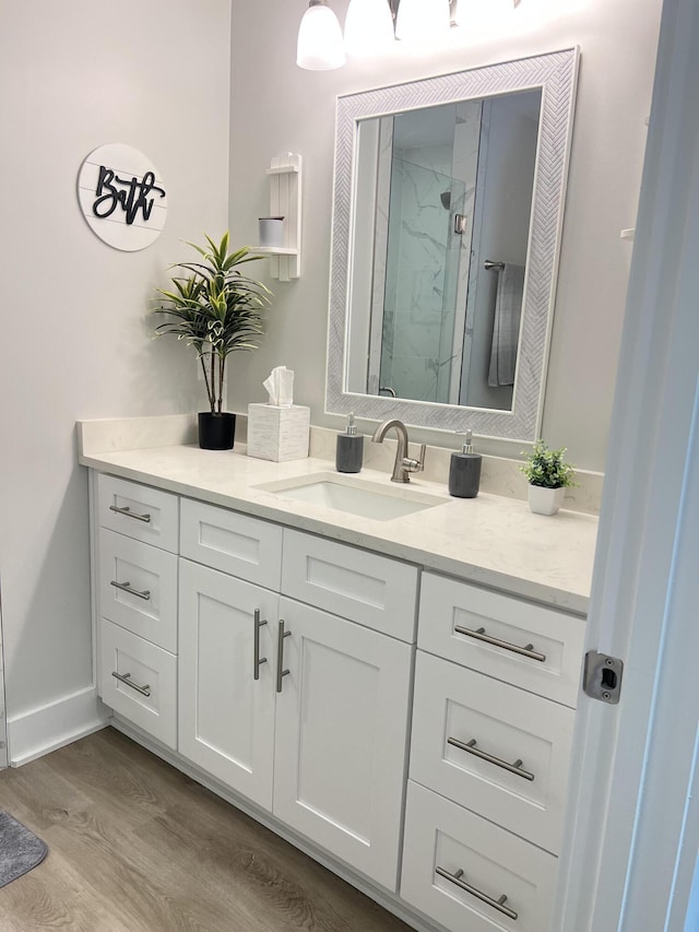 bathroom featuring baseboards, vanity, a marble finish shower, and wood finished floors