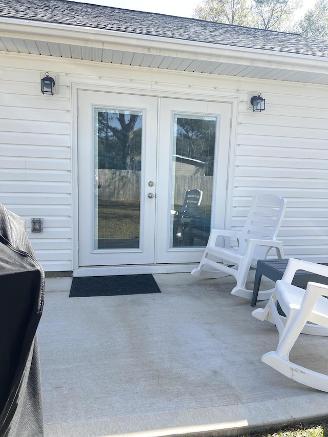 view of exterior entry featuring french doors and a shingled roof