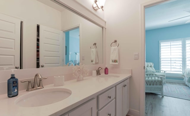 ensuite bathroom featuring double vanity, connected bathroom, wood finished floors, and a sink