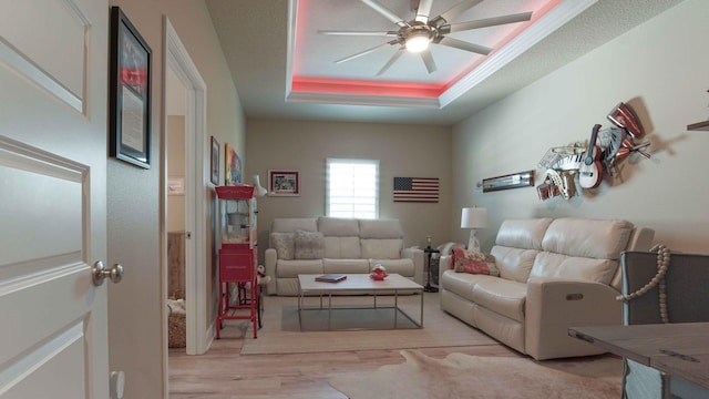 living area with a ceiling fan, a tray ceiling, and wood finished floors