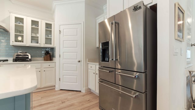 kitchen with light wood finished floors, stainless steel fridge with ice dispenser, white cabinetry, crown molding, and backsplash