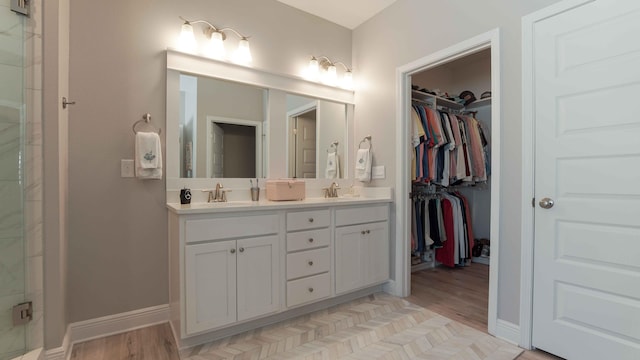 full bathroom featuring a sink, a walk in closet, baseboards, and double vanity