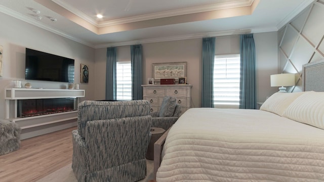 bedroom with a glass covered fireplace, a raised ceiling, wood finished floors, and crown molding