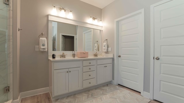 full bath with a sink, baseboards, a shower with door, and double vanity